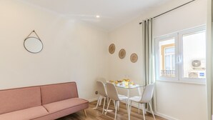 A modern living room with a sofa, a glass dining table with chairs, a round mirror, and three woven wall decorations. - #379 Sunny Corner | Albufeira Stay (Albufeira)