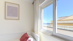 Ein Zimmer mit einem Bett, einem Fenster mit Blick auf ein Gebäude und einem gerahmten Kunstwerk an der Wand.