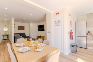 A modern kitchen with a refrigerator, a dining table set with plates, glasses, and a bowl of fruit. - #380 The Sea View Haven | Albufeira (Albufeira)