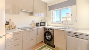 Eine kompakte Küche mit Waschmaschine, Geschirrspüler, Mikrowelle und einem Fenster mit Jalousien.