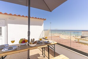 Un balcon avec une table dressée pour deux personnes, un panier de fruits et un verre de vin.