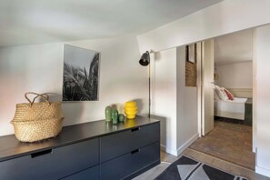 Une chambre moderne avec une commode noire, un panier en osier, un cactus et une lampe.