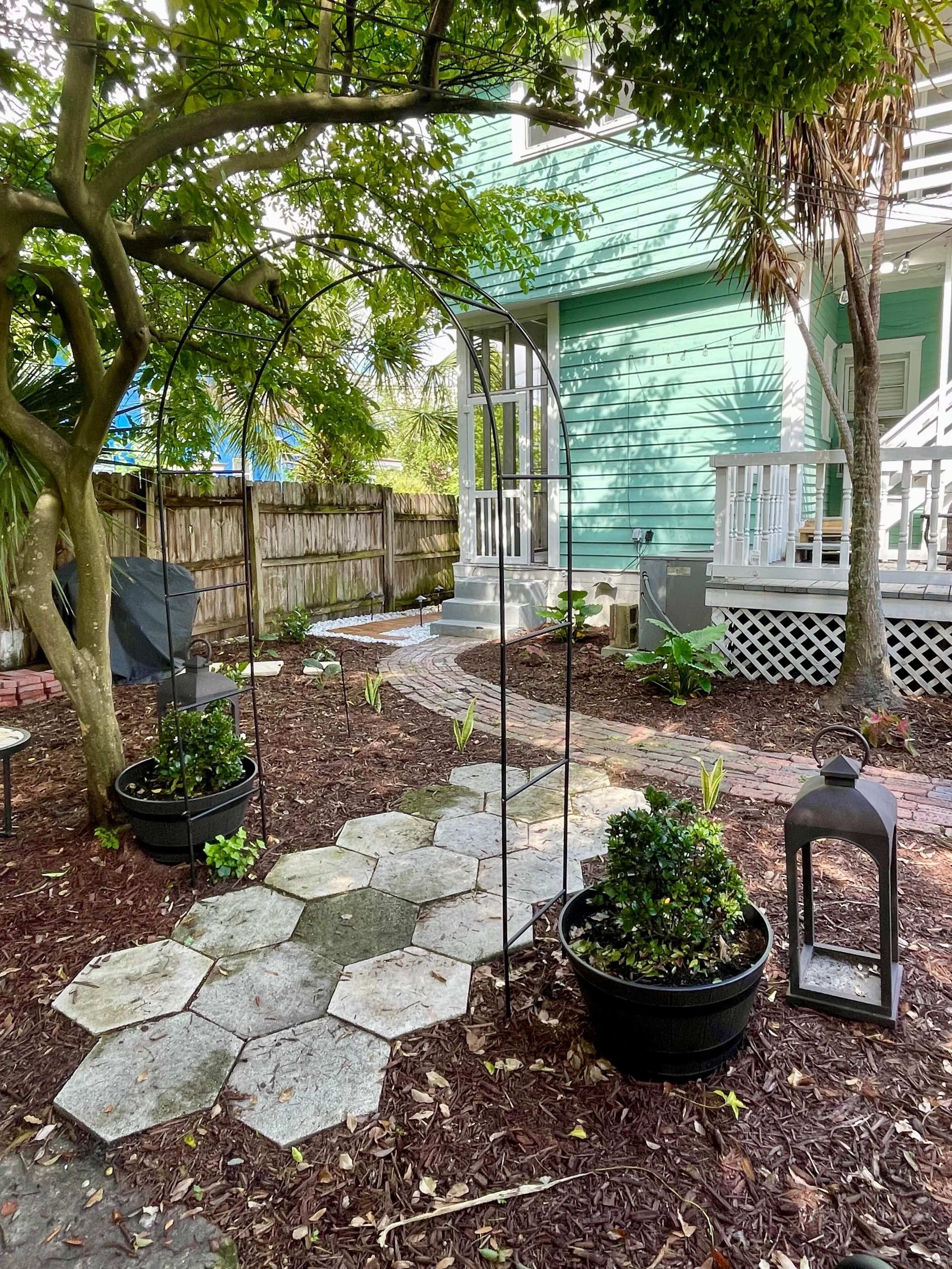 A garden with a stone pathway, potted plants, a pergola, and a wooden fence.