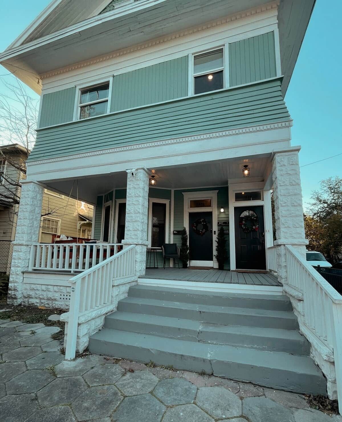 A two-story house with a front porch, steps leading to the entrance, and a small outdoor seating area.