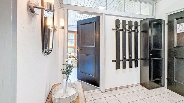 A hallway with a wooden door, a black door, a white wall with a mirror, and a white vase with flowers. - Bernkogel by Interhome (Saalbach-Hinterglemm)