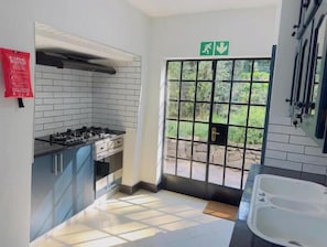 A kitchen with a gas stove, cabinets, and a tiled backsplash. There's a door with a window, a fire extinguisher, and a sign indicating an exit.