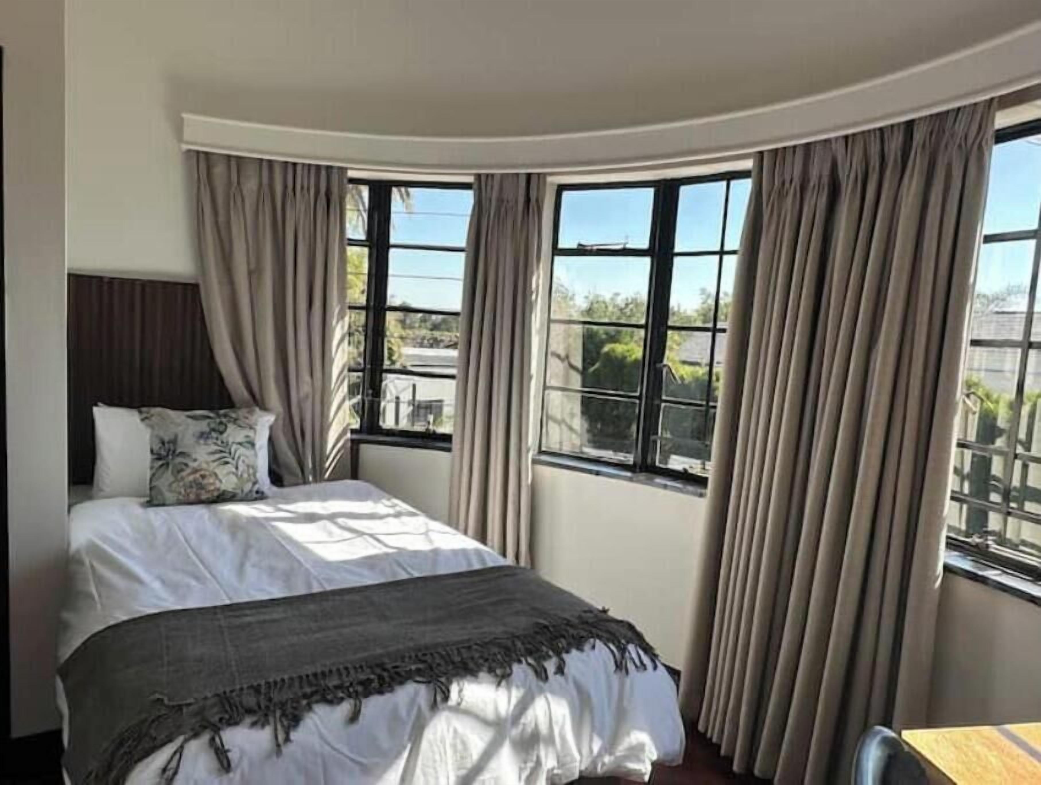 Une chambre à coucher avec un lit, deux fenêtres et des rideaux.