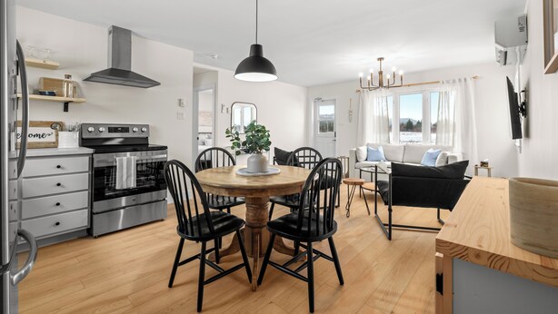 Une cuisine moderne dotée d’appareils électroménagers en acier inoxydable, une table à manger en bois avec des chaises noires et une grande fenêtre agrémentée de rideaux.
