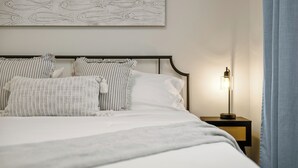 Un lit bien fait, agrémenté d’oreillers à rayures, une lampe de chevet et une décoration murale représentant des poissons.