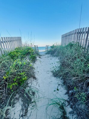 A sandy beach path flanked by wooden fences leading to the sea.