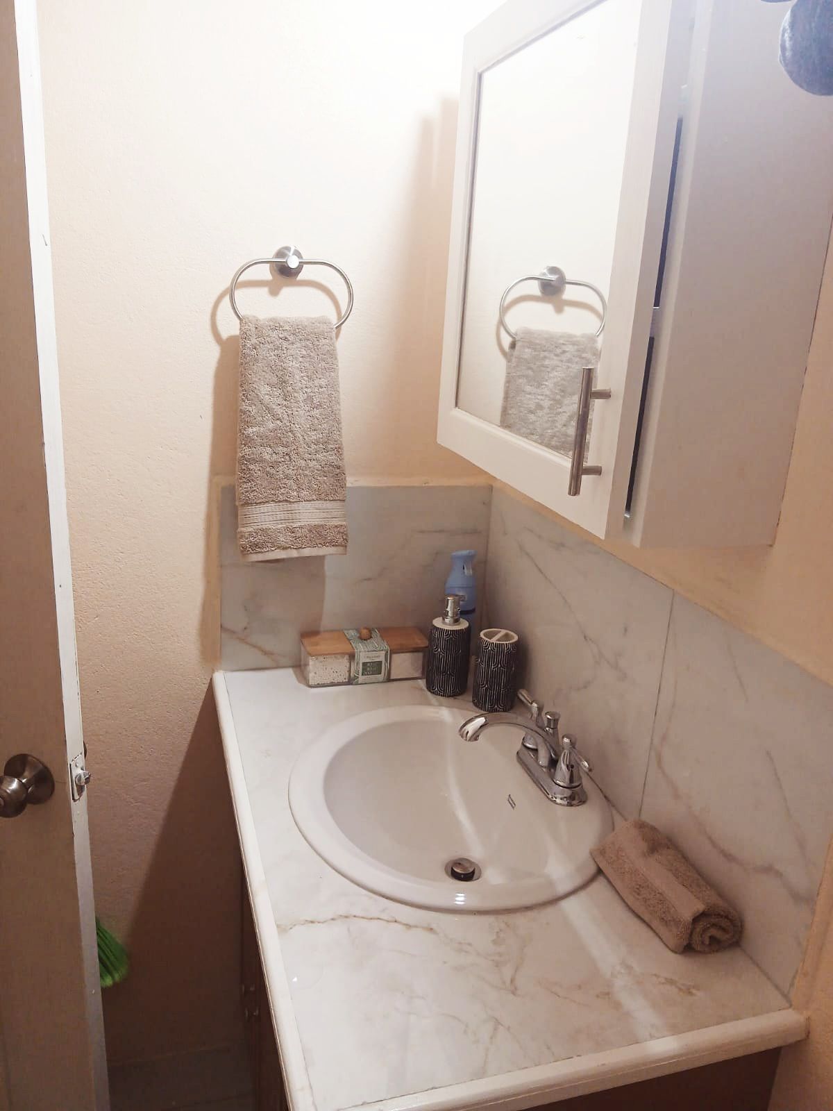 A bathroom with a marble sink, a mirror, a towel rack, and a soap dispenser.