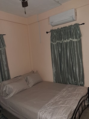 A single bed with a metal frame, a wall-mounted air conditioner, and a ceiling fan.