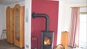 A room with a wood-burning stove, a wooden cabinet, and a chair. - Ferienwohnung in Wenkendorf mit Garten (Fehmarn)