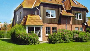 A two-story house with a sloped roof, multiple windows, and a well-maintained lawn. - Ferienwohnung in Wenkendorf mit Garten (Fehmarn)
