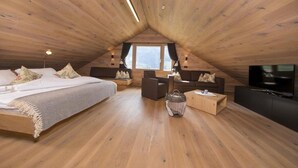 A cozy attic bedroom with a large bed, a TV, and a seating area. - Alpine Stay, Sauna & Fireplace (Bramberg am Wildkogel)