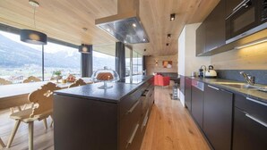 A modern kitchen with a large island, wooden ceiling, and a view of the mountains. - Alpine Stay, Sauna & Fireplace (Bramberg am Wildkogel)