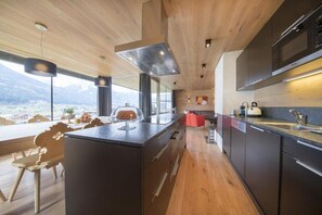 A modern kitchen with a large island, wooden ceiling, and a view of the mountains. - Alpine Stay, Sauna & Fireplace (Bramberg am Wildkogel)