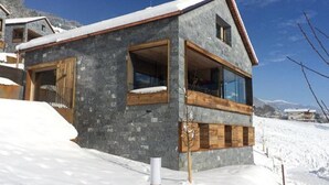 A modern two-story building with large windows, a balcony, and a snow-covered landscape. - Alpine Stay, Sauna & Fireplace (Bramberg am Wildkogel)