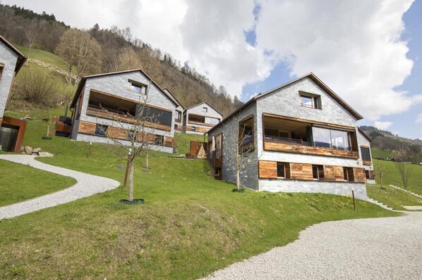 Un chalet moderne avec une façade en pierre, des balcons en bois et une allée gravillonnée.