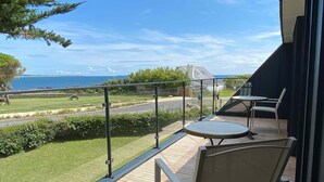 Een balkon met een tafel en stoelen, met uitzicht op een grasveld en een weg.