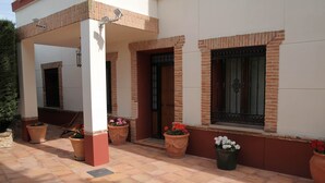 A covered outdoor area with tiled flooring, potted plants, and a brick wall.
