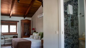A bedroom with a bed, a wooden wardrobe, a window, and a shower with floral wallpaper.