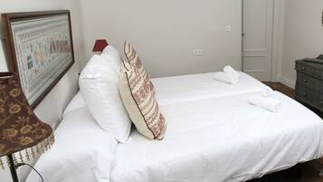 A neatly made bed with white linens, a patterned pillow, a small bedside table with a lamp, and a framed picture on the wall.