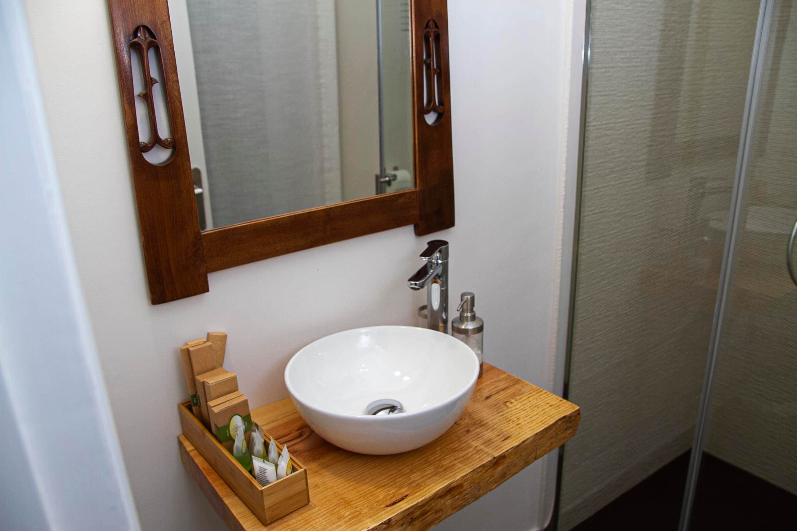 Un baño con tocador de madera, un lavabo blanco, un espejo y cabina de ducha de cristal.