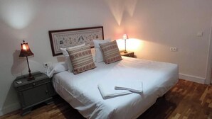 Een slaapkamer met een bed, twee bedlampen, een hanglamp en een ingelijst schilderij aan de muur.