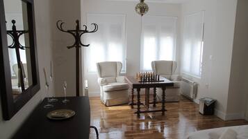 A room with a wooden floor, a chess table, two chairs, a mirror, and a chandelier.