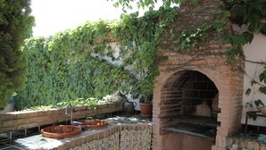 An outdoor kitchen area with a brick oven, tiled flooring, and potted plants.