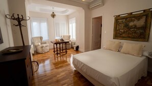 A bedroom with a large bed, a wooden table with chess pieces, two armchairs, and a chandelier.