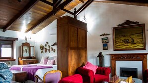 A room with a wooden ceiling, a bed with a purple bedspread, a red sofa, a fireplace, and a painting on the wall.