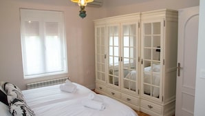 A bedroom with two beds, a large wardrobe, and a window with blinds.
