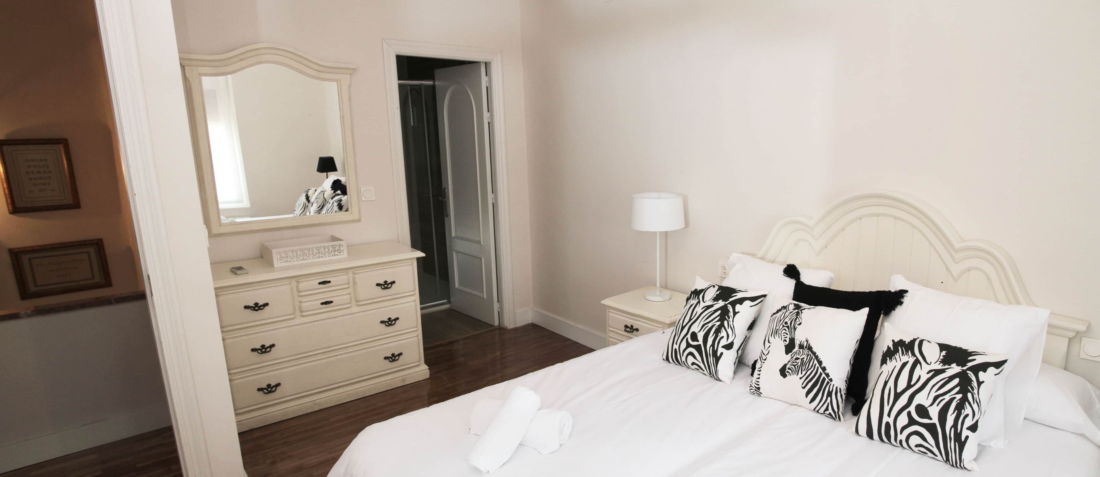 A bedroom with a bed, a dresser, a mirror, a nightstand, and a lamp.