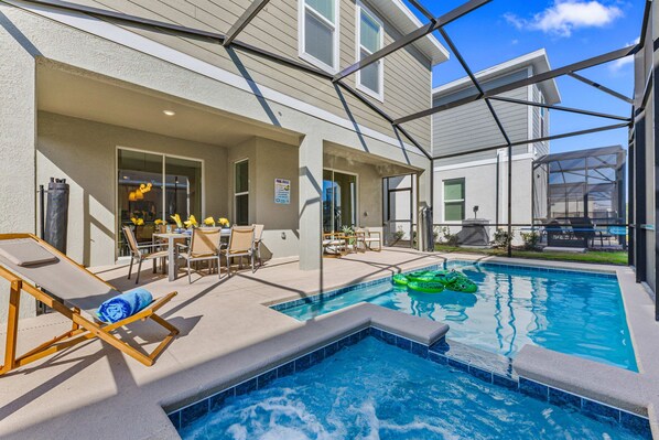 Una piscina con cerramiento de vidrio, mobiliario exterior y zona de patio.