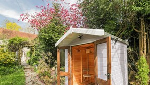 A wooden sauna with a glass door, surrounded by a garden with a stone pathway. - Lavender Cottage (Gillingham)