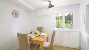 A dining room with a wooden table, chairs, a clock, and a window with a view of greenery. - Lavender Cottage (Gillingham)