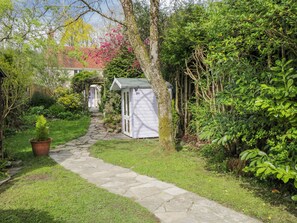 A stone pathway leading to a white shed in a lush garden with various plants and a house in the background. - Lavender Cottage (Gillingham)