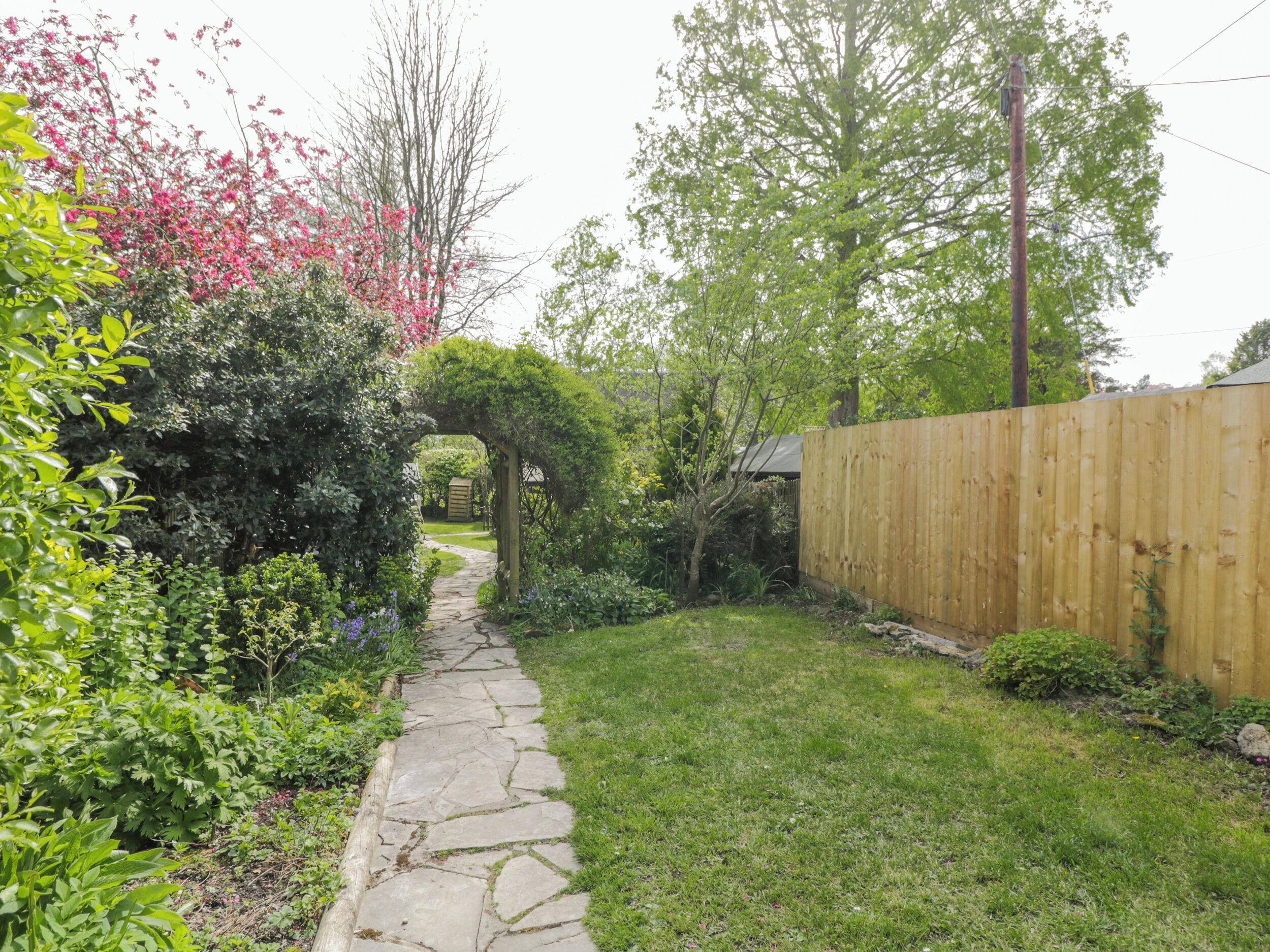 A stone pathway leading through a garden with a wooden fence and greenery.