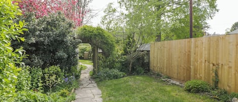 A stone pathway leading through a garden with a wooden fence and greenery.