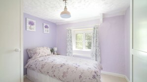 A bedroom with a bed, a window with curtains, and wall art. - Lavender Cottage (Gillingham)