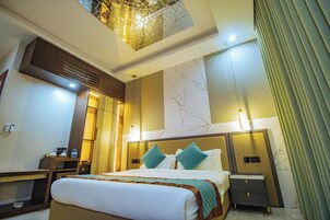 Habitación de hotel con una cama grande, mesitas de noche, un escritorio, una silla, un espejo, una ventana con cortinas y una lámpara en el techo.