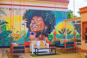 Una habitación con un mural, muebles de mimbre y una silla colgante.