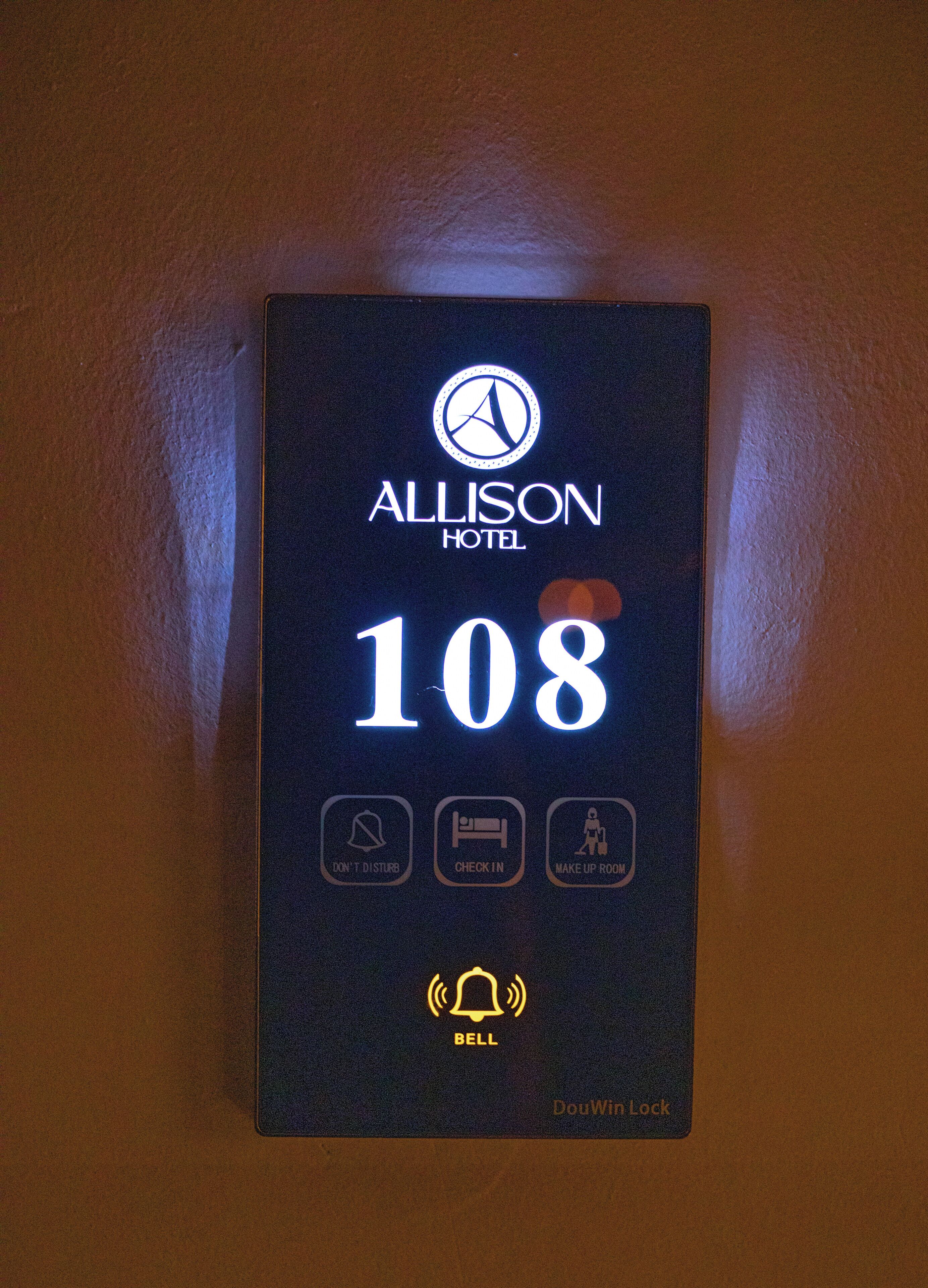 Une plaque indiquant le numéro de chambre de l’hôtel Allison, chambre 108, avec des icônes représentant les services offerts, comme une sonnette, un service d’enregistrement et un service de préparation de la chambre.