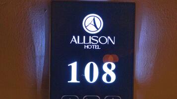 Une plaque indiquant le numéro de chambre de l’hôtel Allison, chambre 108, avec des icônes représentant les services offerts, comme une sonnette, un service d’enregistrement et un service de préparation de la chambre.
