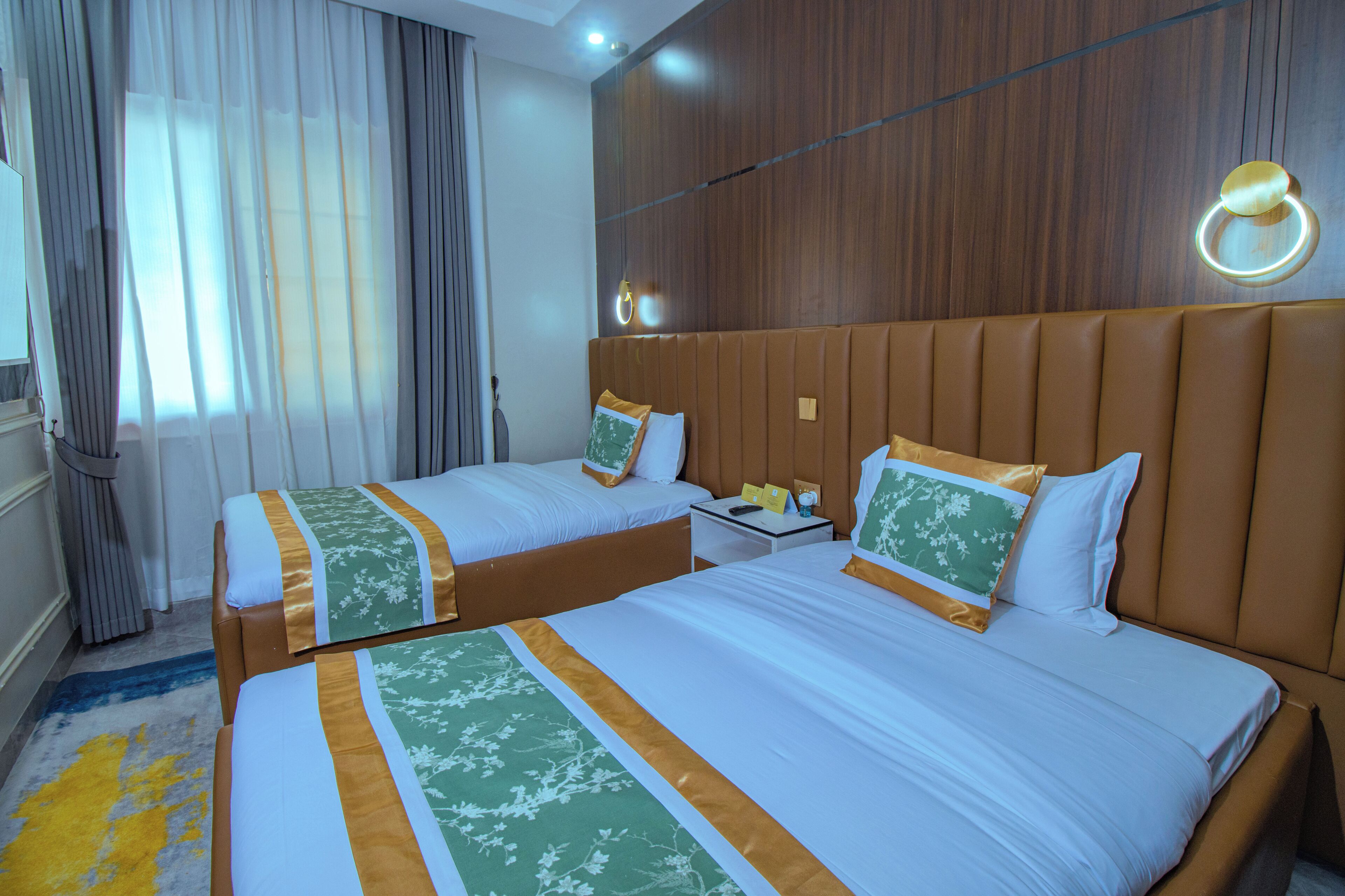 A hotel room with two beds, a wooden headboard, a nightstand, and a window with curtains.