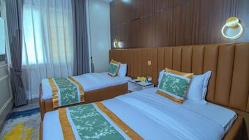 A hotel room with two beds, a wooden headboard, a nightstand, and a window with curtains.