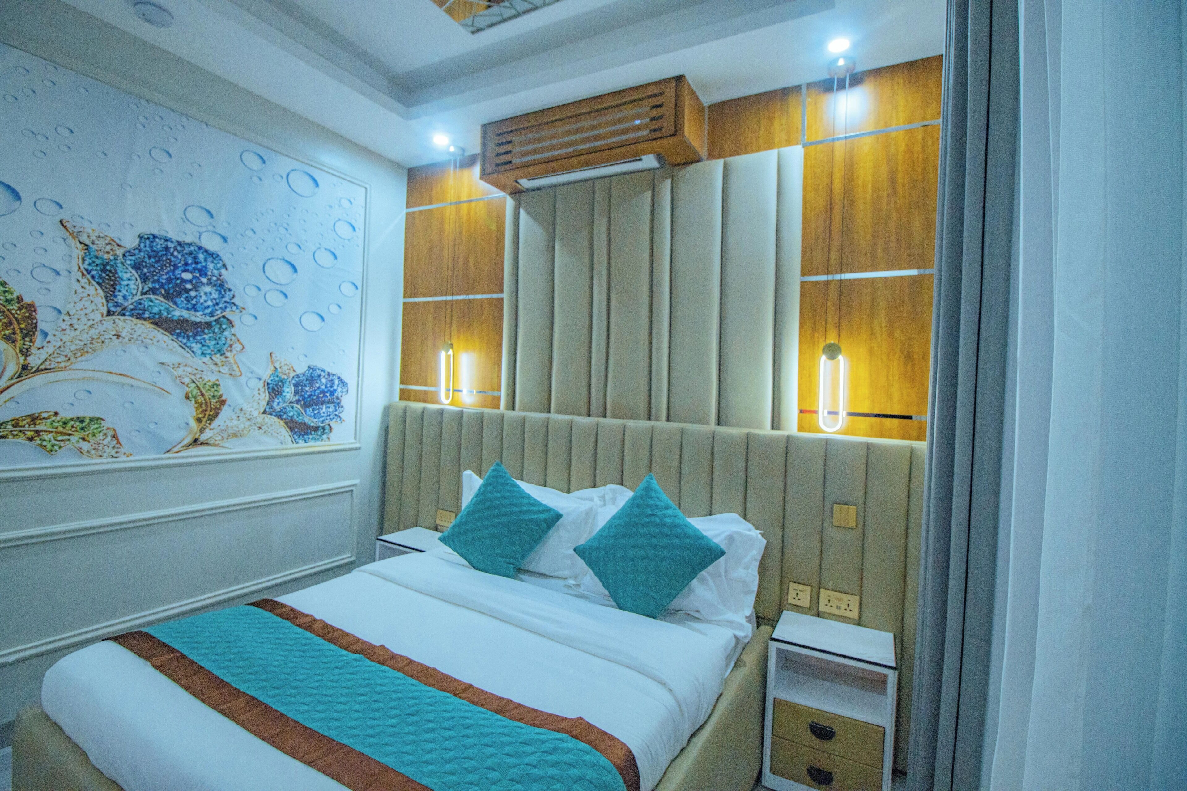 A hotel room with a bed, nightstand, wall art, and a mirror.