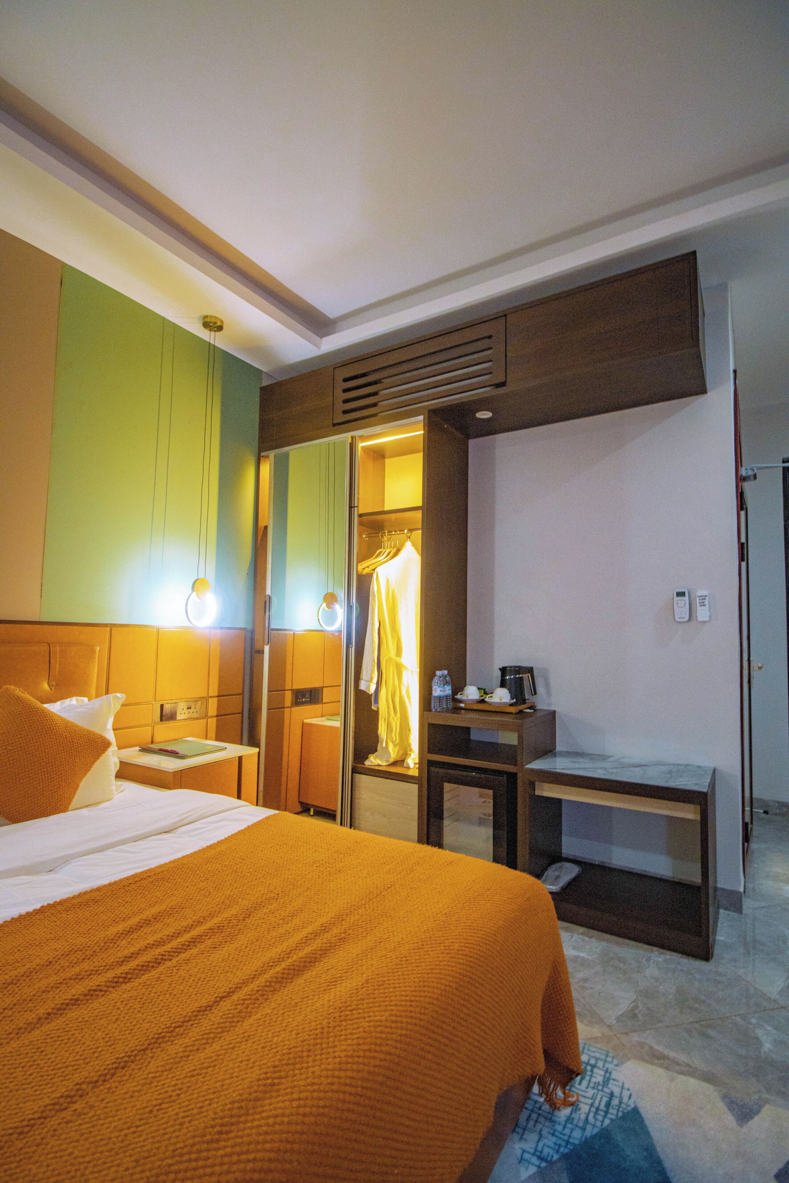 A hotel room with a bed, bedside table, a mirror, a desk, and a wardrobe.